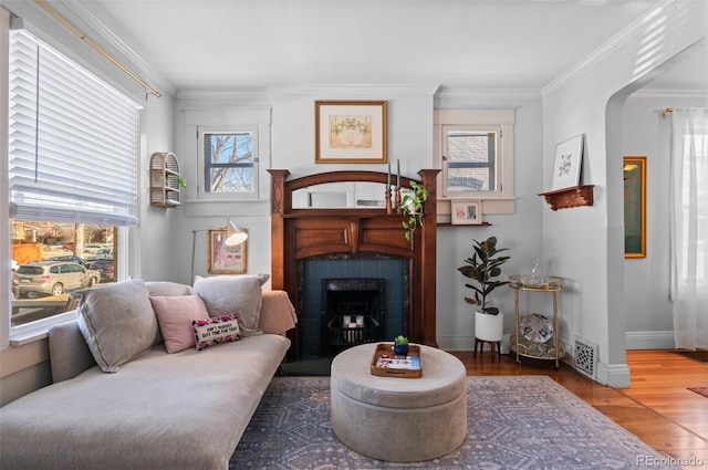 living area featuring ornamental molding, a tile fireplace, and wood-type flooring