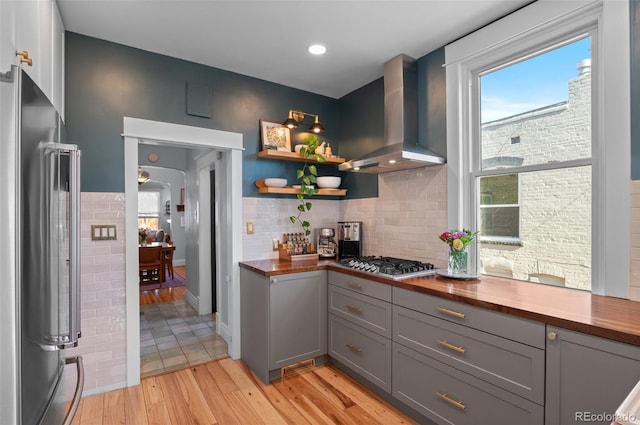 kitchen with gray cabinets, tasteful backsplash, stainless steel appliances, light wood-type flooring, and wall chimney exhaust hood