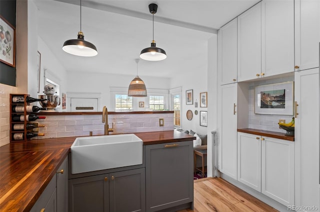 kitchen with sink, wooden counters, white cabinetry, backsplash, and decorative light fixtures