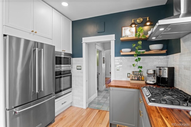 kitchen with island exhaust hood, wooden counters, stainless steel appliances, and white cabinets