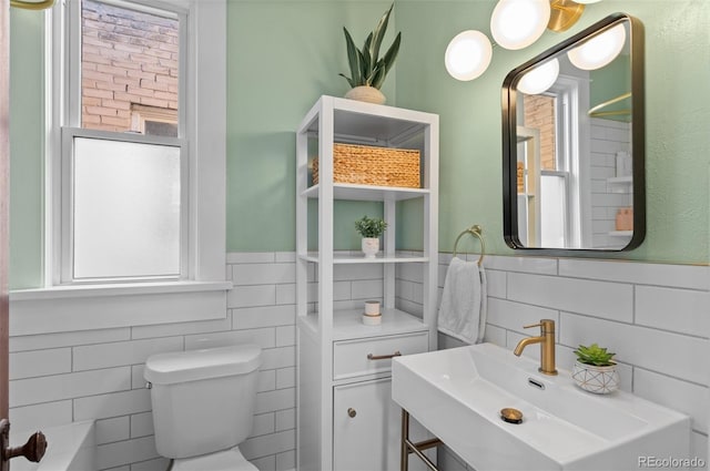 bathroom with toilet, sink, tile walls, and a tub