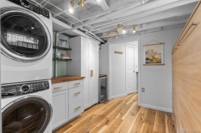 washroom featuring wine cooler, light hardwood / wood-style flooring, cabinets, and stacked washer / dryer