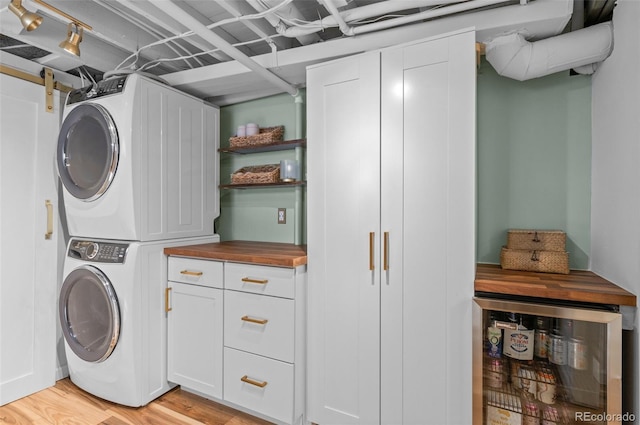 laundry area with cabinets, light hardwood / wood-style flooring, beverage cooler, and stacked washing maching and dryer