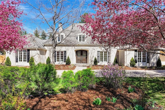 view of front of home with brick siding, french doors, and a chimney