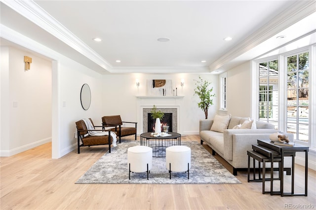 living room with a warm lit fireplace, crown molding, a tray ceiling, and light wood-style floors