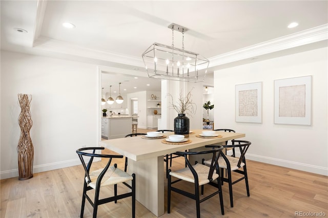 dining area with crown molding, a chandelier, light wood-type flooring, a tray ceiling, and baseboards