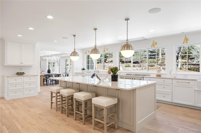 kitchen featuring light stone counters, a breakfast bar, a center island with sink, light wood-style flooring, and white cabinets