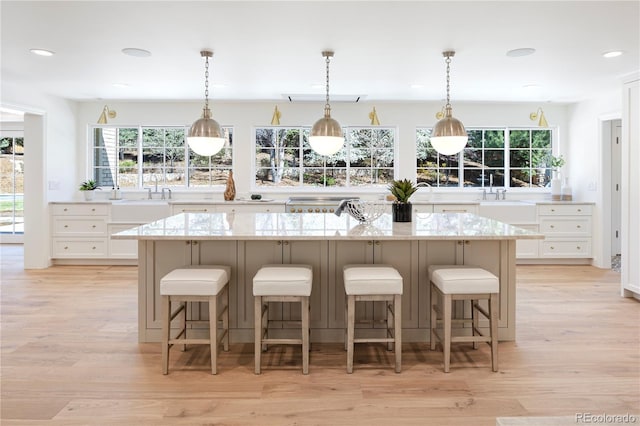 kitchen with a kitchen breakfast bar, a sink, light wood finished floors, white cabinetry, and light stone countertops