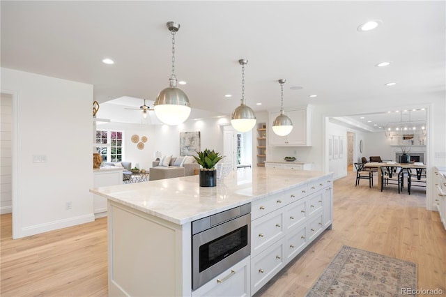 kitchen featuring stainless steel microwave, a kitchen island, light wood-style flooring, open floor plan, and white cabinetry