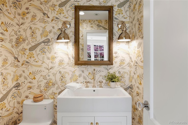 half bath with toilet, vanity, and wallpapered walls