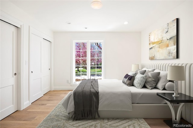 bedroom featuring light wood-style flooring, baseboards, recessed lighting, and two closets