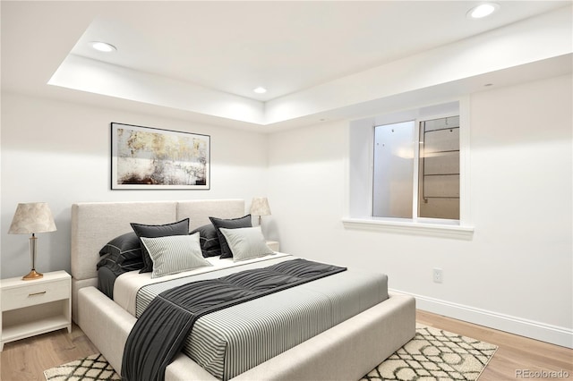 bedroom with recessed lighting, light wood-style floors, baseboards, and a raised ceiling