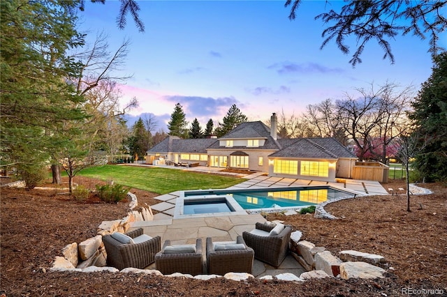 pool at dusk with a yard, an outdoor pool, a patio area, and an in ground hot tub