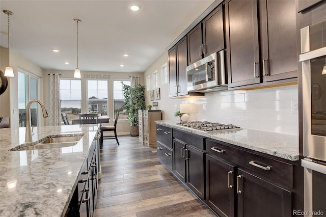 kitchen featuring pendant lighting, sink, appliances with stainless steel finishes, dark brown cabinets, and light stone countertops