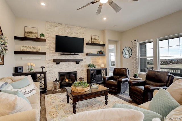 living room featuring a stone fireplace, wood-type flooring, and ceiling fan