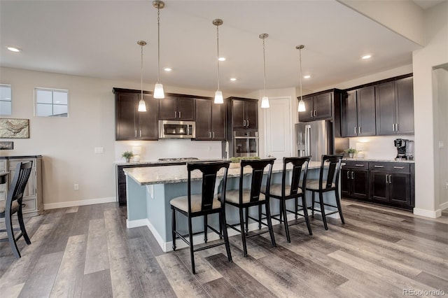 kitchen featuring stainless steel appliances, a center island with sink, pendant lighting, and a kitchen bar