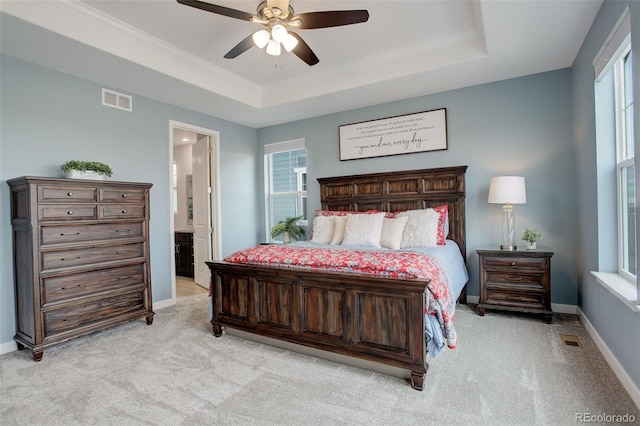 carpeted bedroom with crown molding, a tray ceiling, ceiling fan, and ensuite bathroom