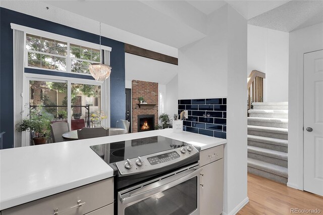2021 S Hannibal Way Unit F, Aurora, CO 80013 - kitchen with stainless steel electric range, light countertops, a brick fireplace, a chandelier, and light wood-type flooring