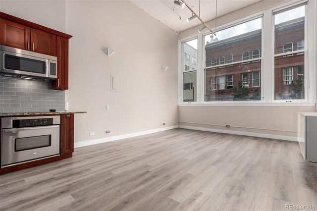 720 16th St Unit 207, Denver, CO 80202 - kitchen featuring stainless steel appliances, light wood-style flooring, decorative backsplash, lofted ceiling, and light stone counters