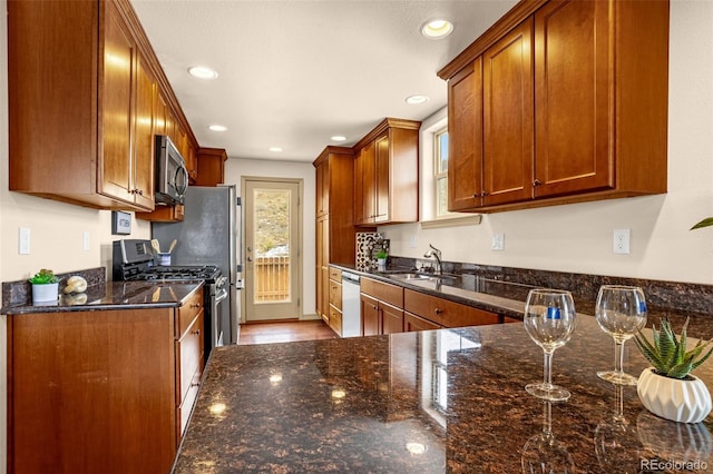 kitchen with dark stone counters, brown cabinetry, recessed lighting, a sink, and stainless steel appliances