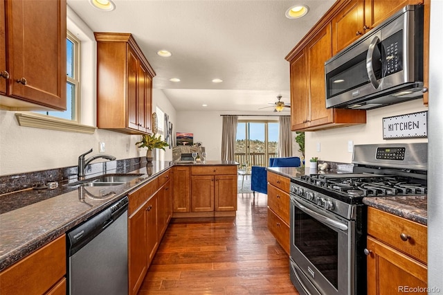 kitchen with brown cabinetry, appliances with stainless steel finishes, a sink, and dark wood finished floors