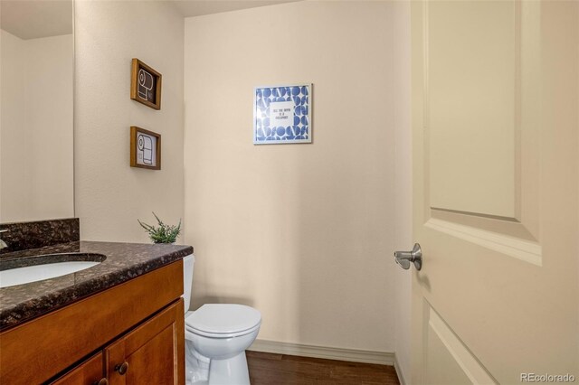 half bathroom featuring toilet, wood finished floors, vanity, and baseboards