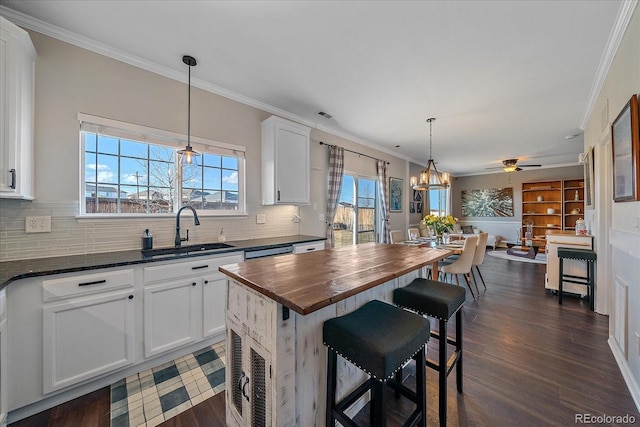 kitchen with butcher block counters, a kitchen island, sink, and white cabinets