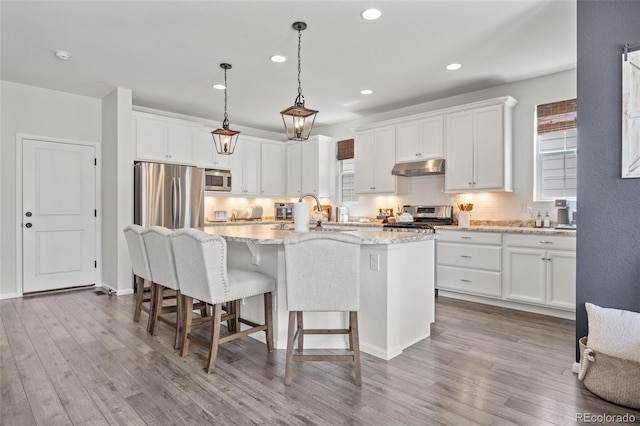 3535 Raintree Ln, Dacono, CO 80514 - kitchen with stainless steel appliances, under cabinet range hood, an island with sink, a kitchen bar, and decorative backsplash