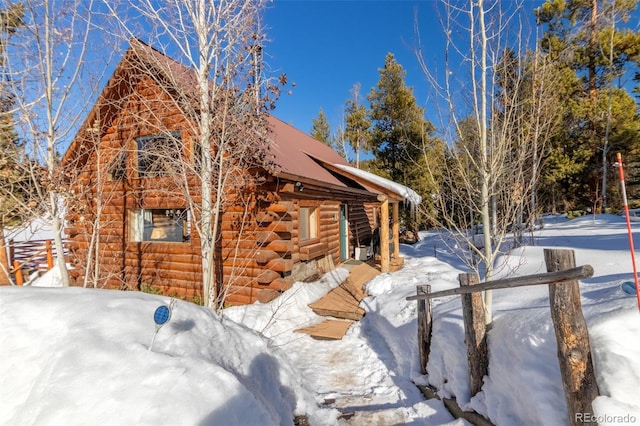 view of snowy exterior featuring log exterior and heating fuel