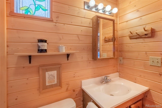 bathroom featuring wooden walls, toilet, and vanity