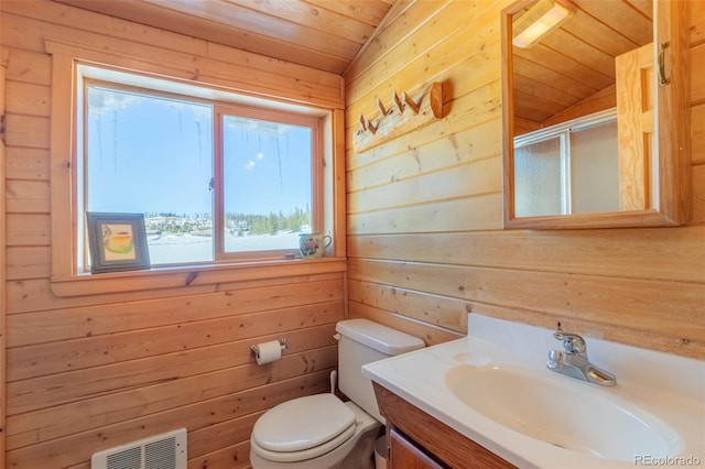 full bath featuring a stall shower, visible vents, toilet, vanity, and wood walls