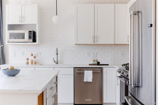 kitchen with premium appliances, white cabinetry, a sink, and backsplash