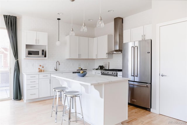 kitchen featuring white cabinetry, appliances with stainless steel finishes, a center island, wall chimney exhaust hood, and a kitchen bar