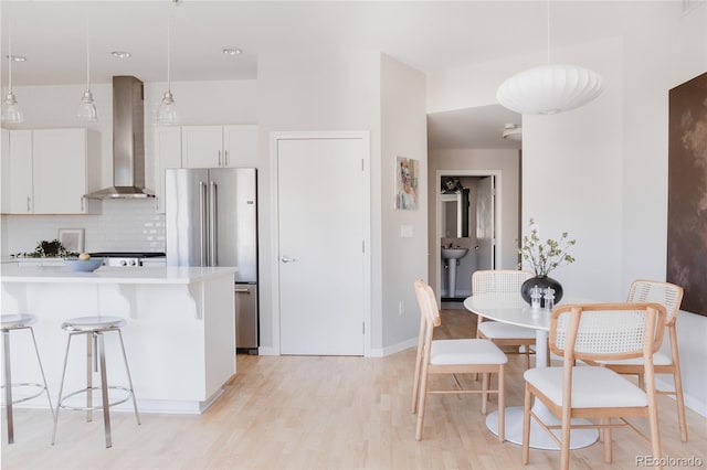 kitchen featuring tasteful backsplash, high quality fridge, a kitchen breakfast bar, light wood-type flooring, and wall chimney range hood