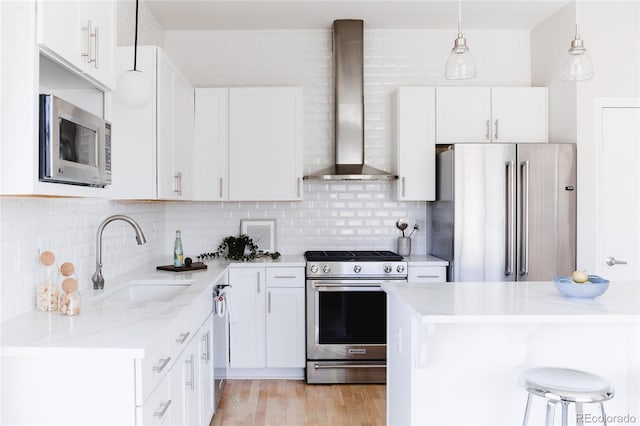 kitchen featuring appliances with stainless steel finishes, a sink, wall chimney range hood, white cabinetry, and backsplash