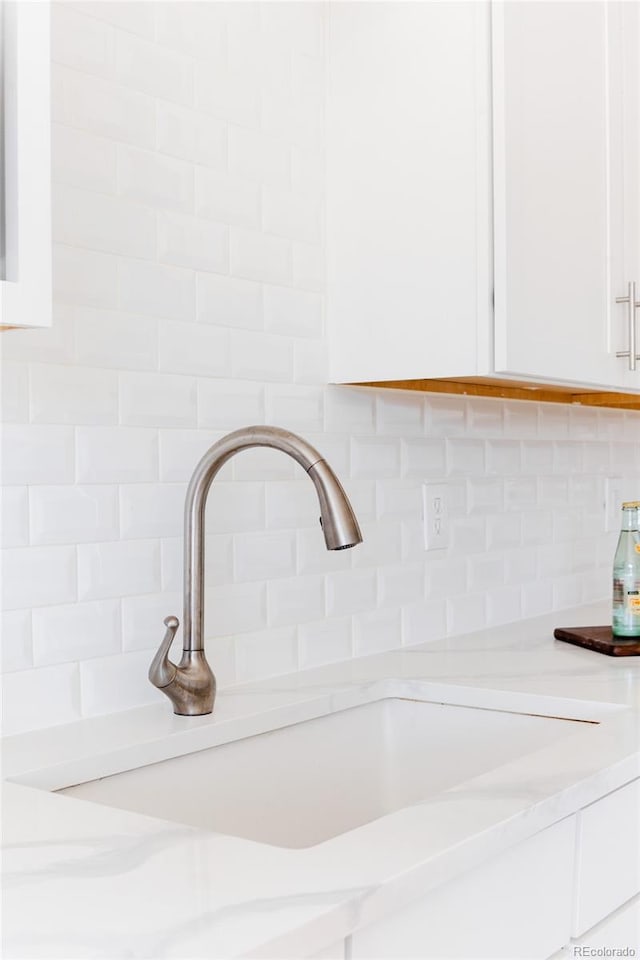 interior details featuring decorative backsplash, white cabinets, a sink, and light countertops