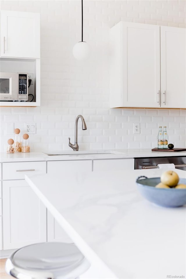 kitchen featuring tasteful backsplash, white cabinets, light countertops, and white microwave