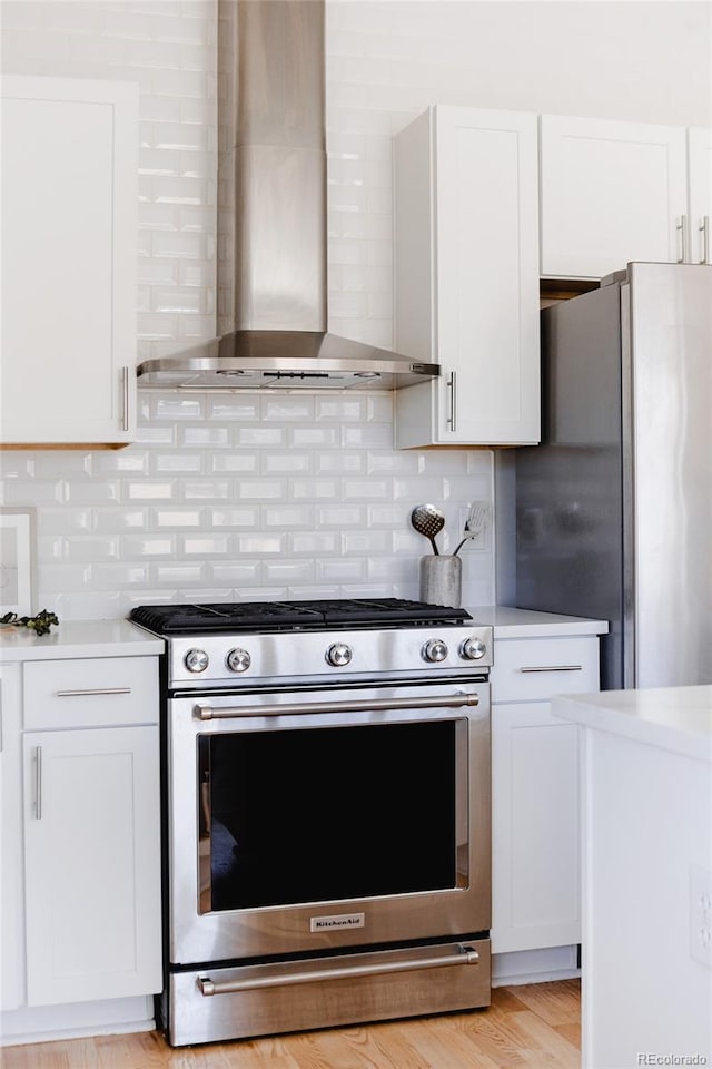 kitchen featuring appliances with stainless steel finishes, light countertops, wall chimney range hood, and white cabinetry