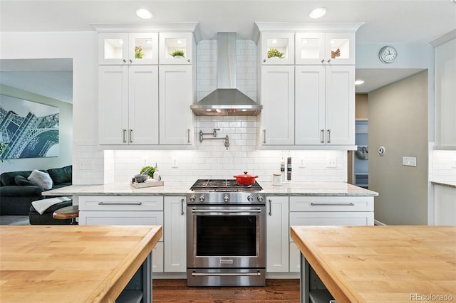 kitchen with stainless steel range with gas cooktop, wall chimney range hood, butcher block countertops, and glass insert cabinets