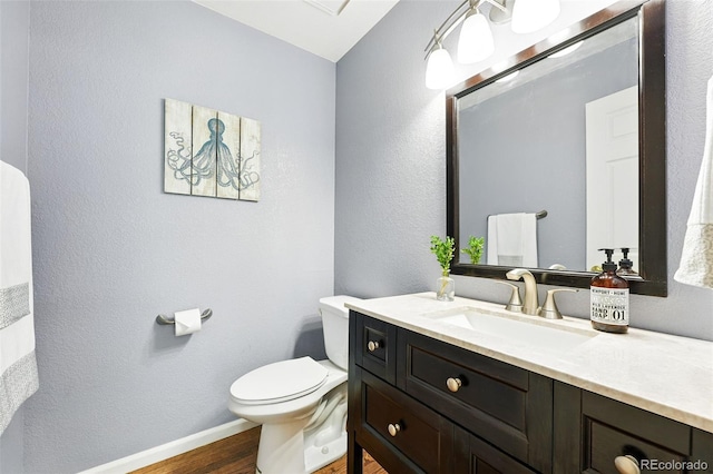 half bathroom featuring toilet, wood finished floors, vanity, a textured wall, and baseboards