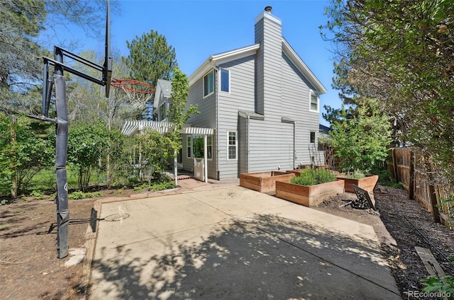 rear view of property featuring fence, a patio, a garden, and a chimney