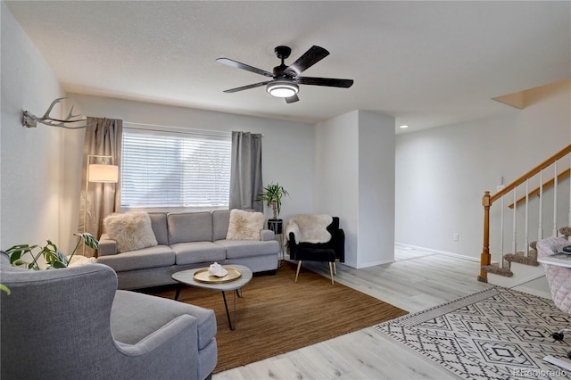 living area with light wood finished floors, stairway, a ceiling fan, a textured ceiling, and baseboards