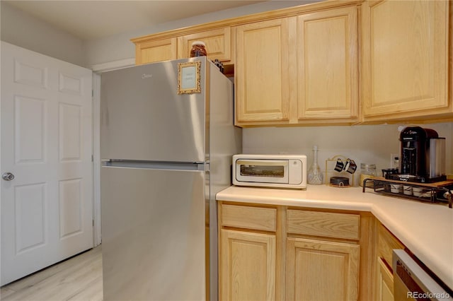 kitchen featuring a toaster, light brown cabinets, dishwasher, and freestanding refrigerator