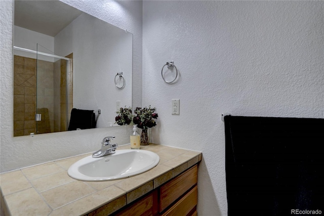 full bathroom featuring a stall shower, a textured wall, and vanity