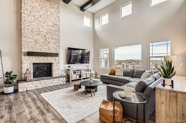 living room with a high ceiling, a stone fireplace, wood finished floors, and beam ceiling