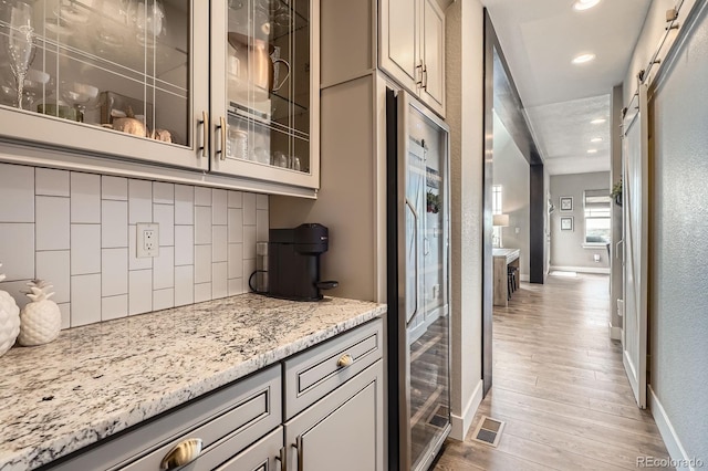 kitchen with baseboards, glass insert cabinets, light wood finished floors, and tasteful backsplash