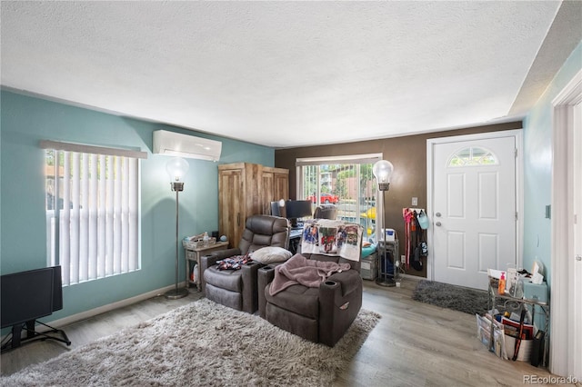 living room with a textured ceiling, a wall mounted AC, light wood-type flooring, and baseboards