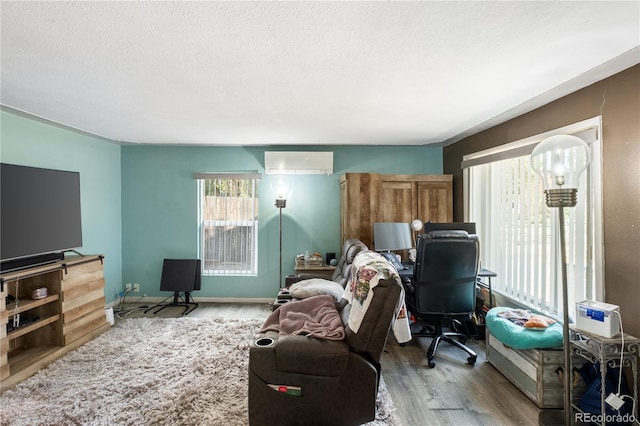 living room featuring a wall unit AC, a textured ceiling, baseboards, and wood finished floors