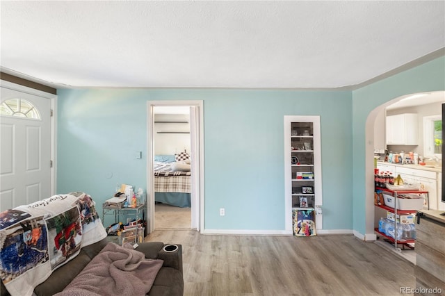 interior space featuring light wood-style floors, arched walkways, a textured ceiling, and baseboards