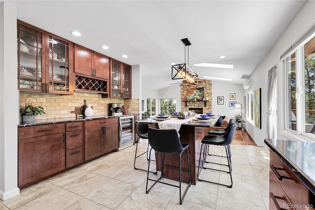 bar with hanging light fixtures, beverage cooler, a stone fireplace, decorative backsplash, and lofted ceiling